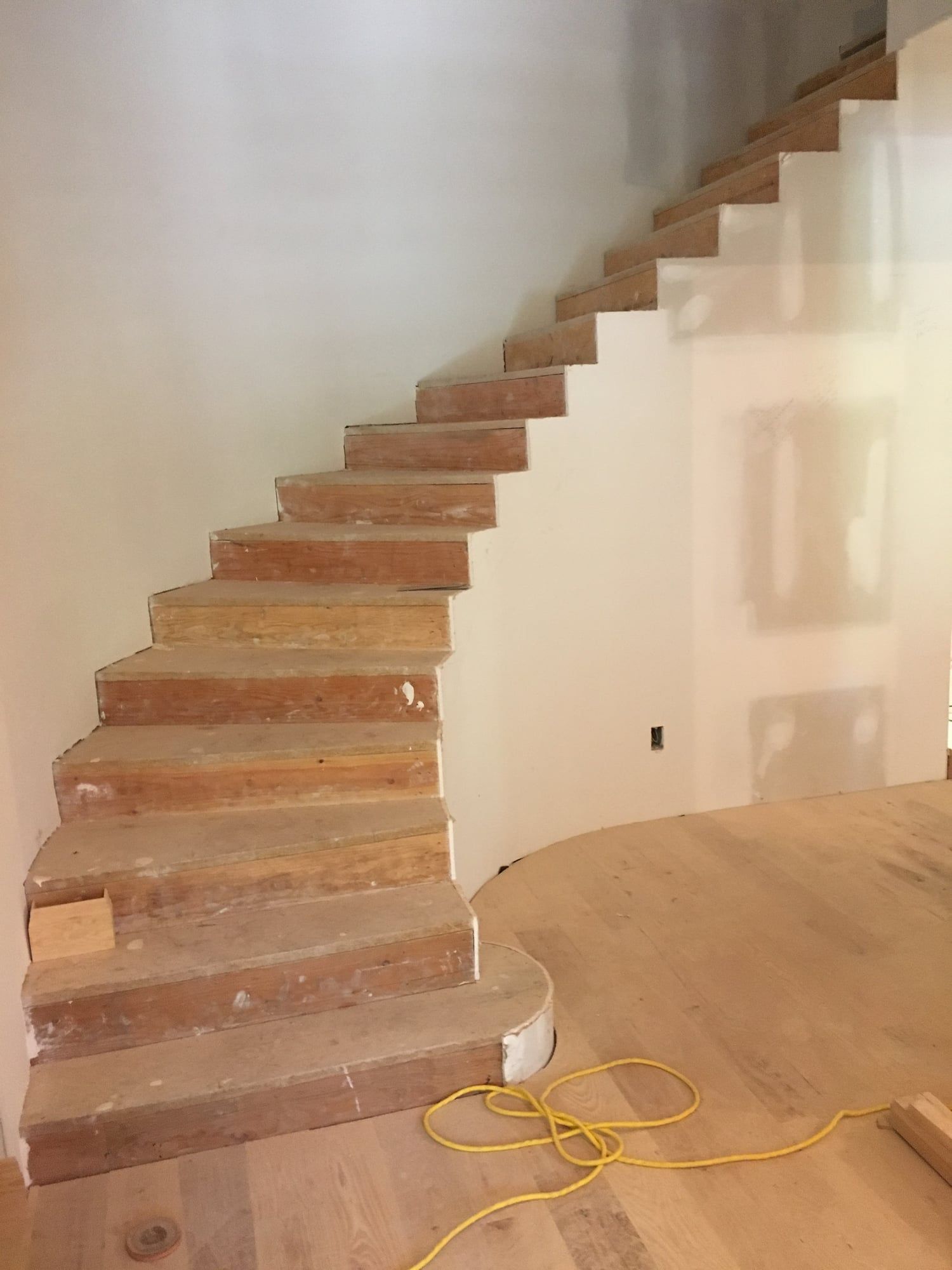 Curved staircase mid-construction, cut to a tight radius with temporary plywood treads in place before the finish stair and drywall are completed
