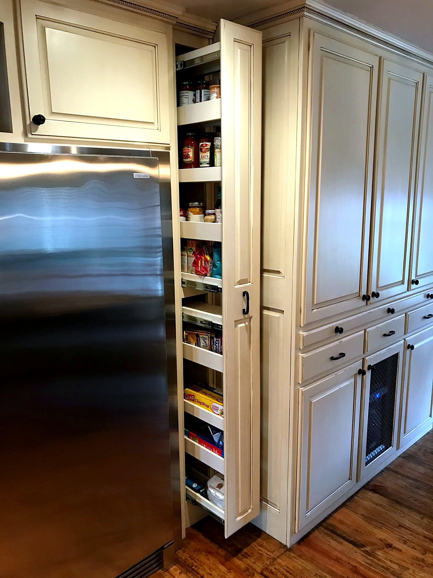 Pull-out pantry cabinet extended beside a built-in stainless refrigerator, cream cabinetry