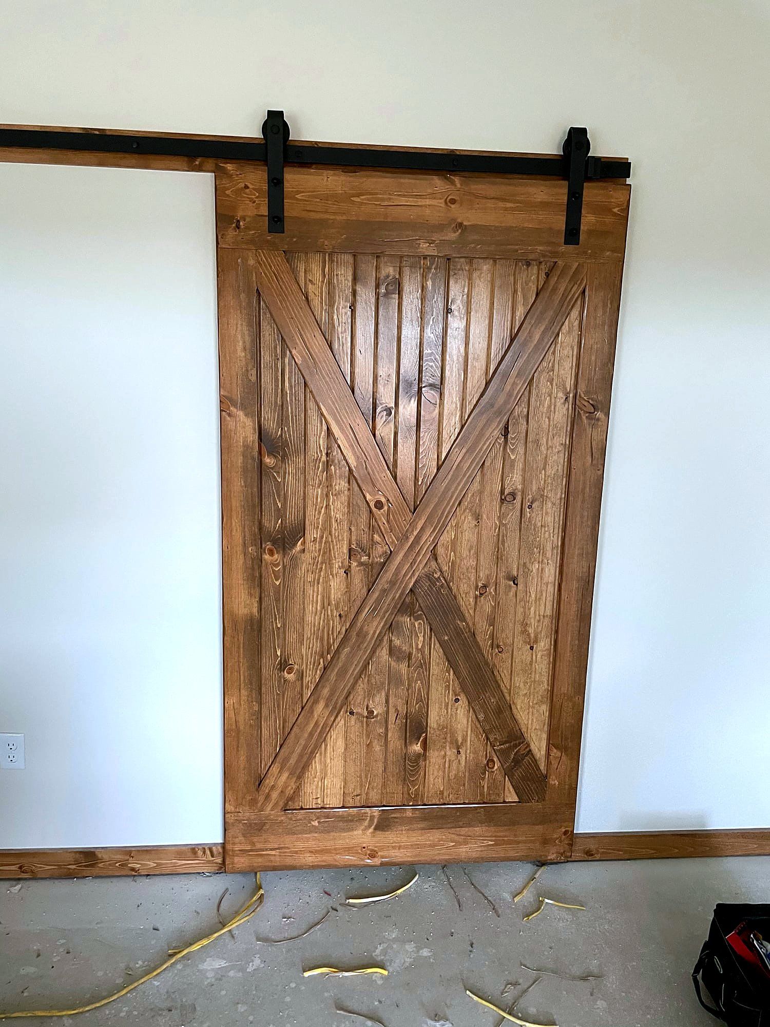 Natural wood sliding barn door with an X-brace pattern and black barn-door hardware