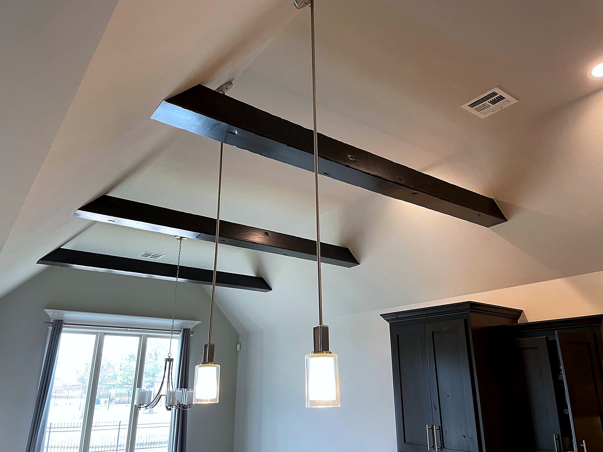 Vaulted living room ceiling with dark exposed wood beams and pendant lighting over dark cabinetry