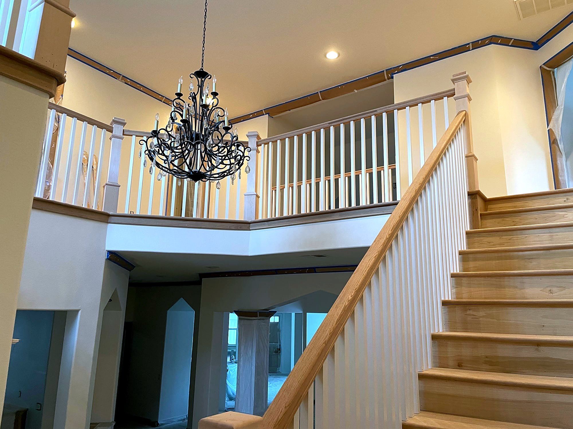 Curved two-story stairwell with a wood handrail and a wrought iron chandelier overhead