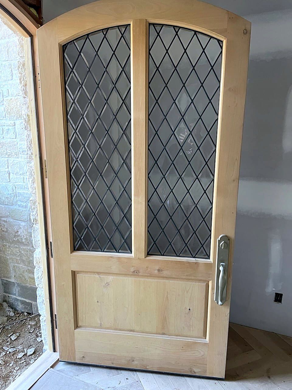 Arched entry door with diamond-pattern leaded glass, natural finish, hung in a stone-and-stucco entryway