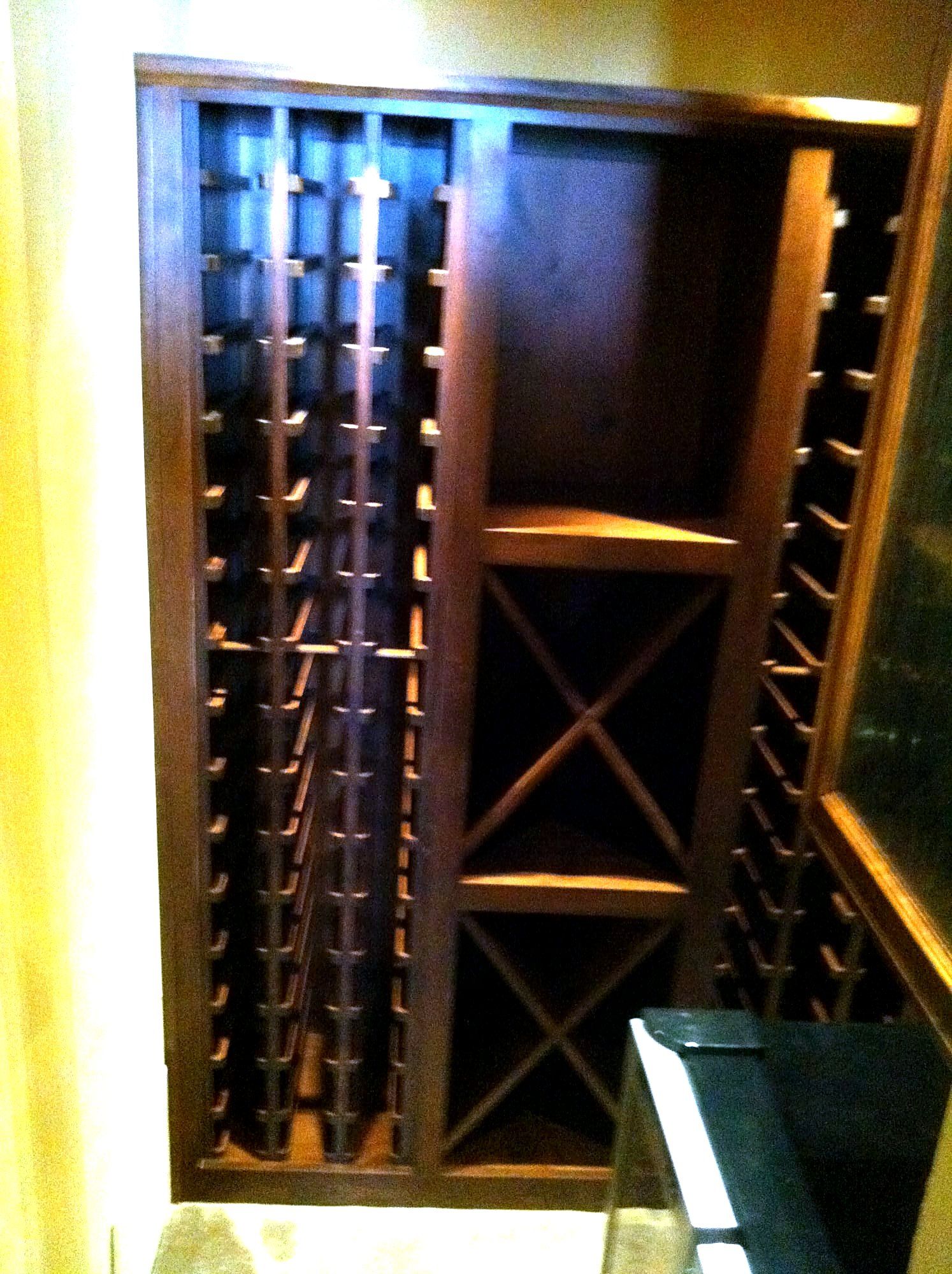 Dark wood wine storage cabinet with diagonal X-shaped bottle racks, lit from within